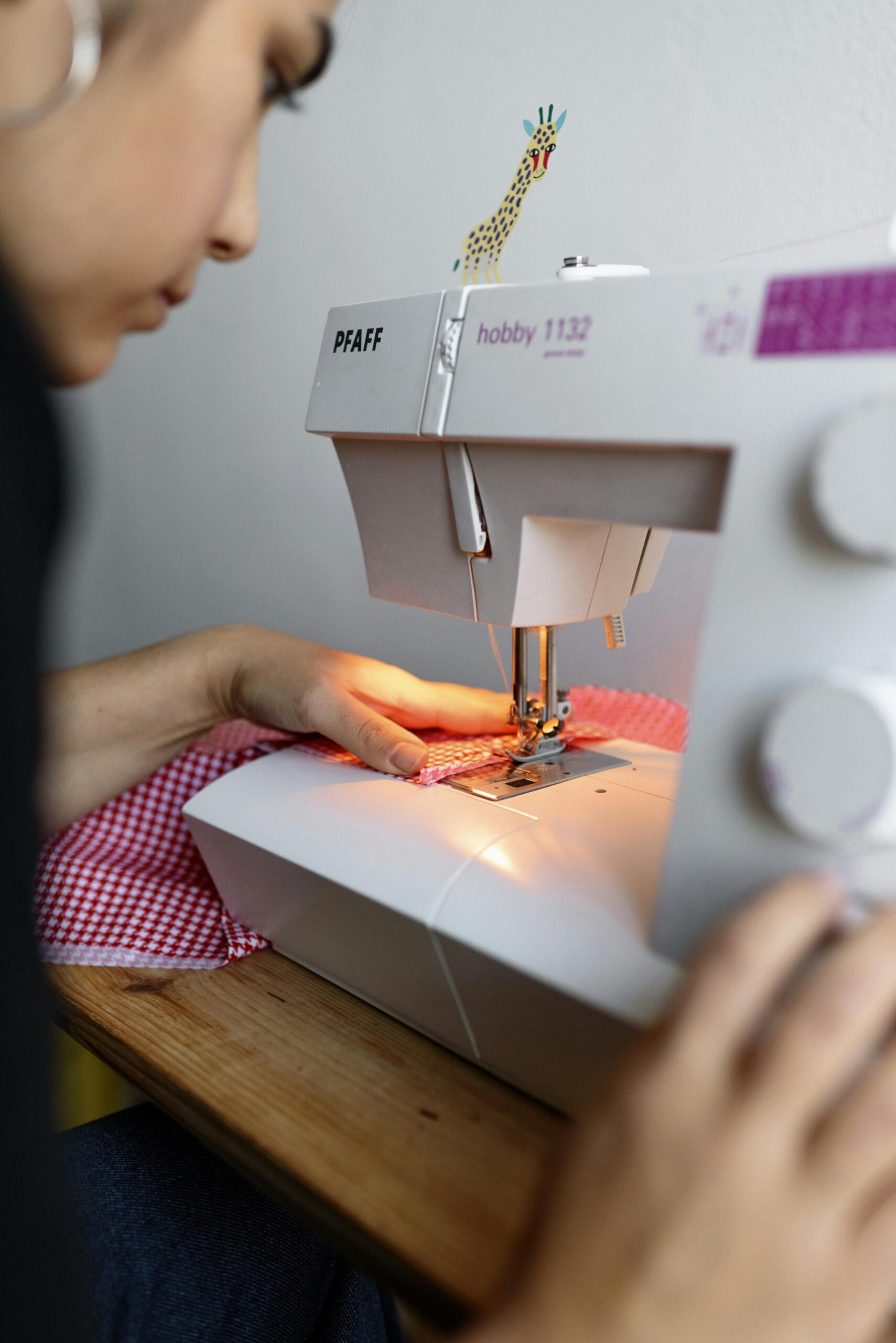 Home Close-up of a woman sewing fabric on a Pfaff sewing machine in a creative studio setting.